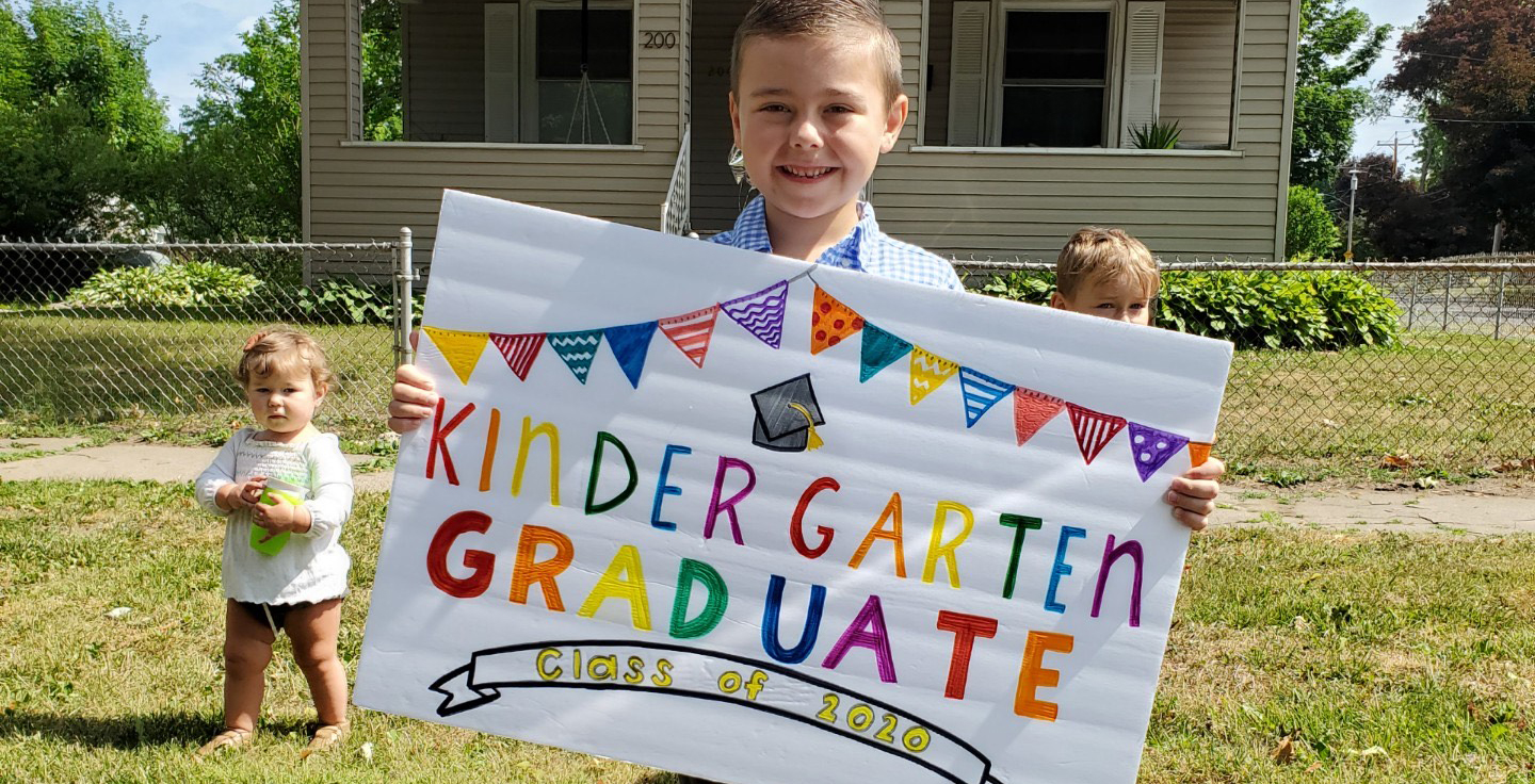 UAS Scholar smiles with Kindergarten Graduation Sign
